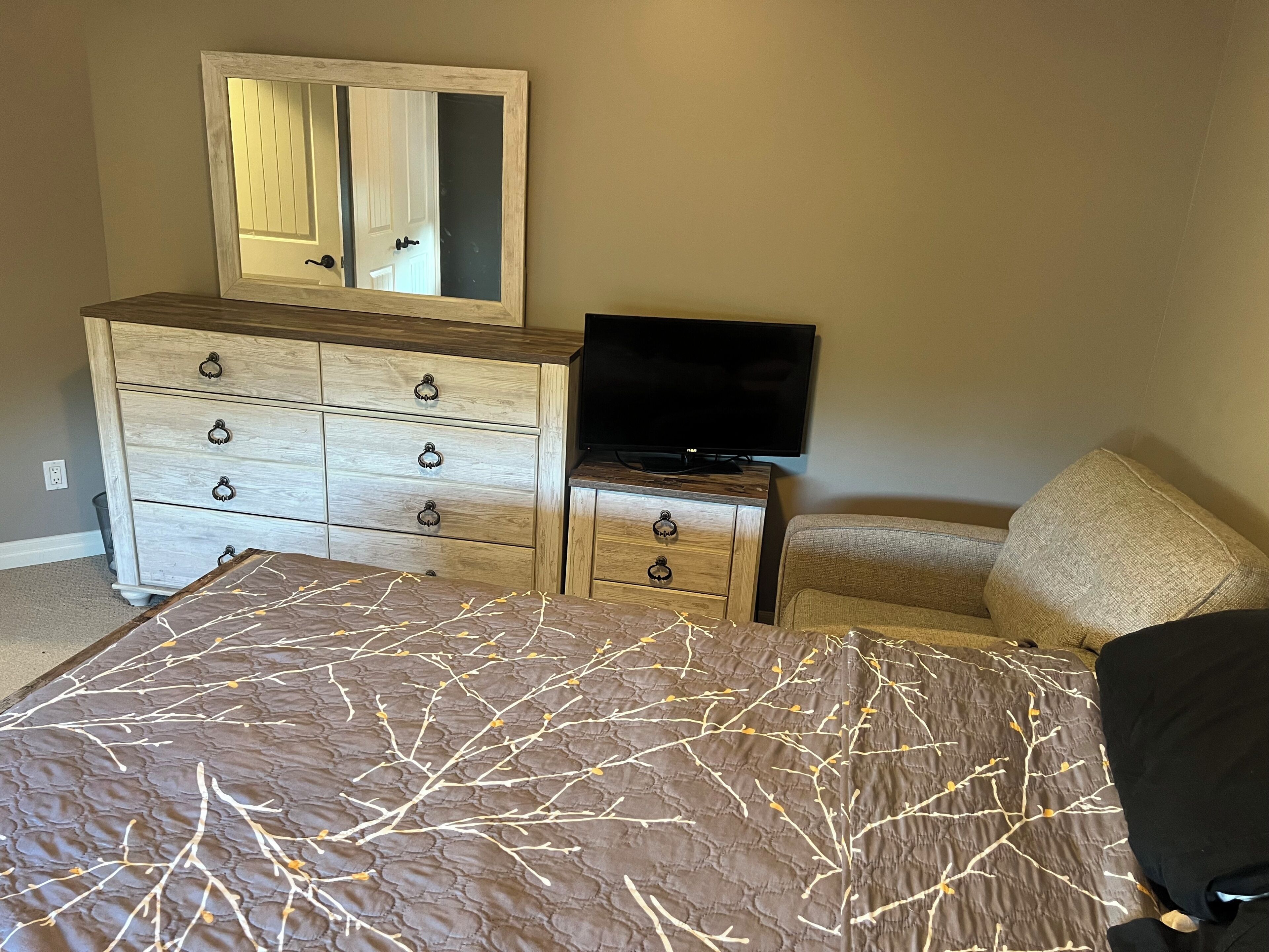A bedroom with a bed, dresser, television, and a mirror.