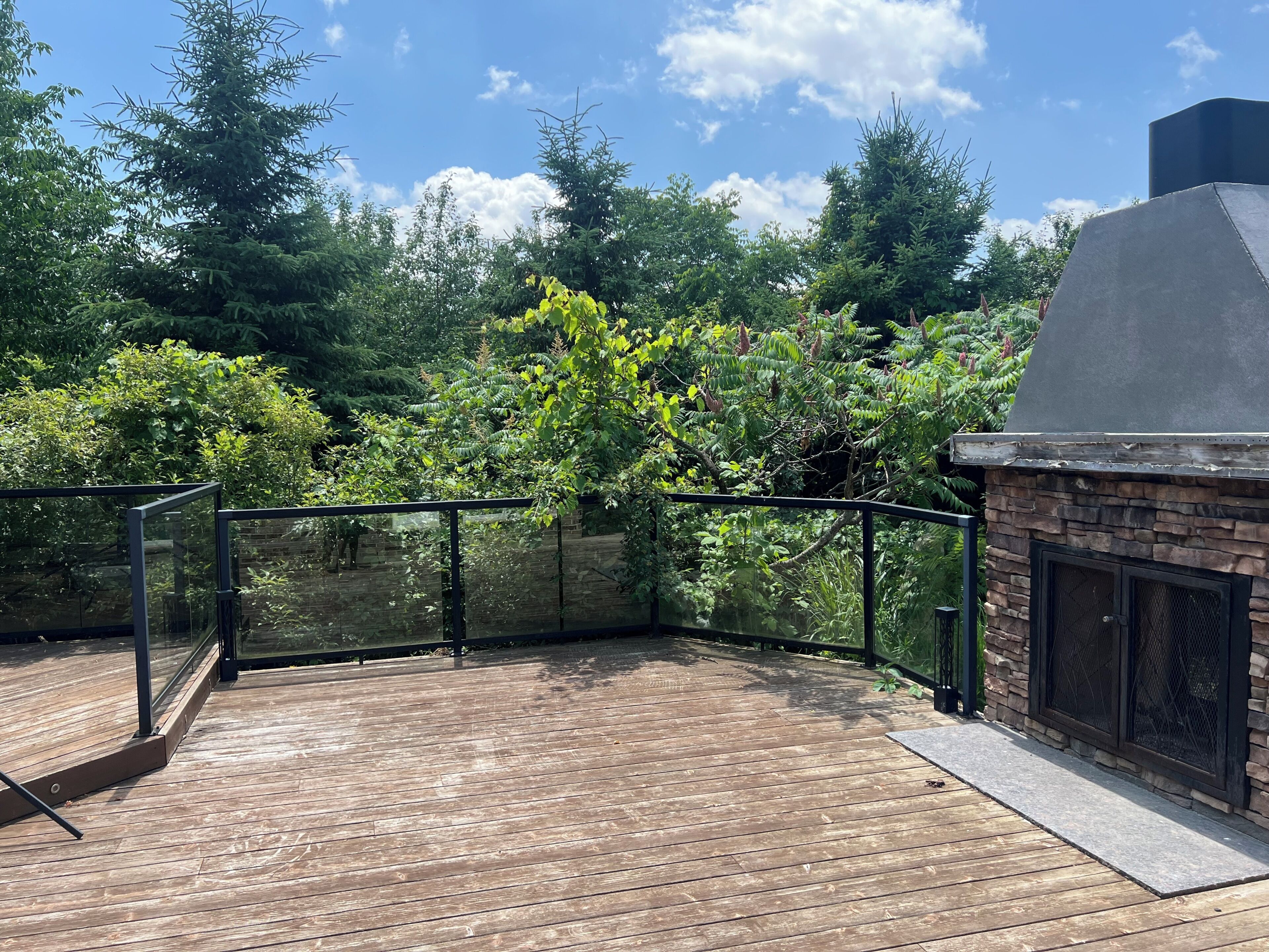 A wooden deck with a stone fireplace and a metal railing.
