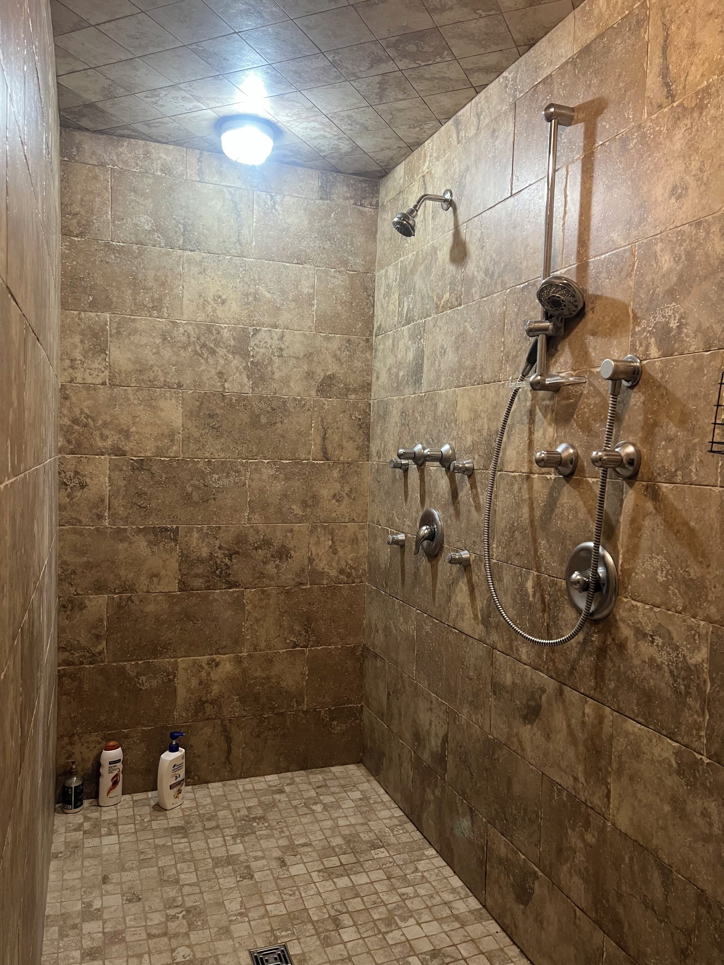 A shower with a handheld showerhead and a wall-mounted showerhead, both with hoses.