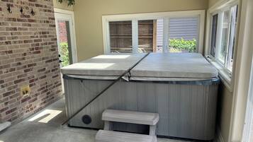 A room with a brick wall, a window with blinds, a small step leading to a bench, and a hot tub.