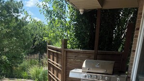 Ein Grill und Ofen auf einer Holzterrasse, mit einem Holenzaun und Grünpflanzen im Hintergrund.