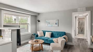 A modern living room with a teal sofa, a round wooden coffee table, and a white armchair.