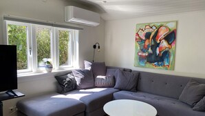 Ein modernes Wohnzimmer mit einem grauen Ecksofa, einem weißen runden Couchtisch und einem farbenfrohen abstrakten Gemälde an der Wand.
