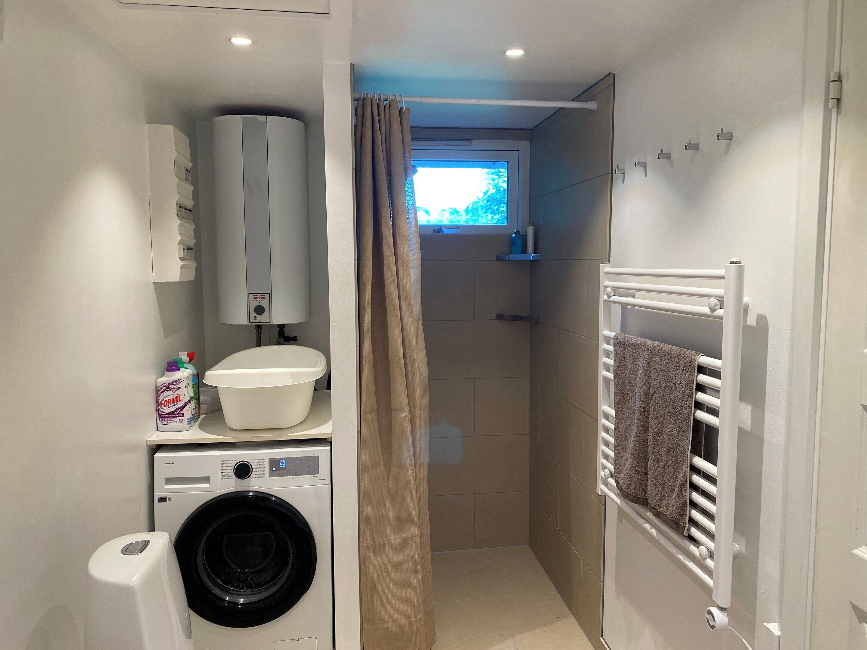 A compact bathroom with a washing machine, a toilet, a shower area, and a towel rack.