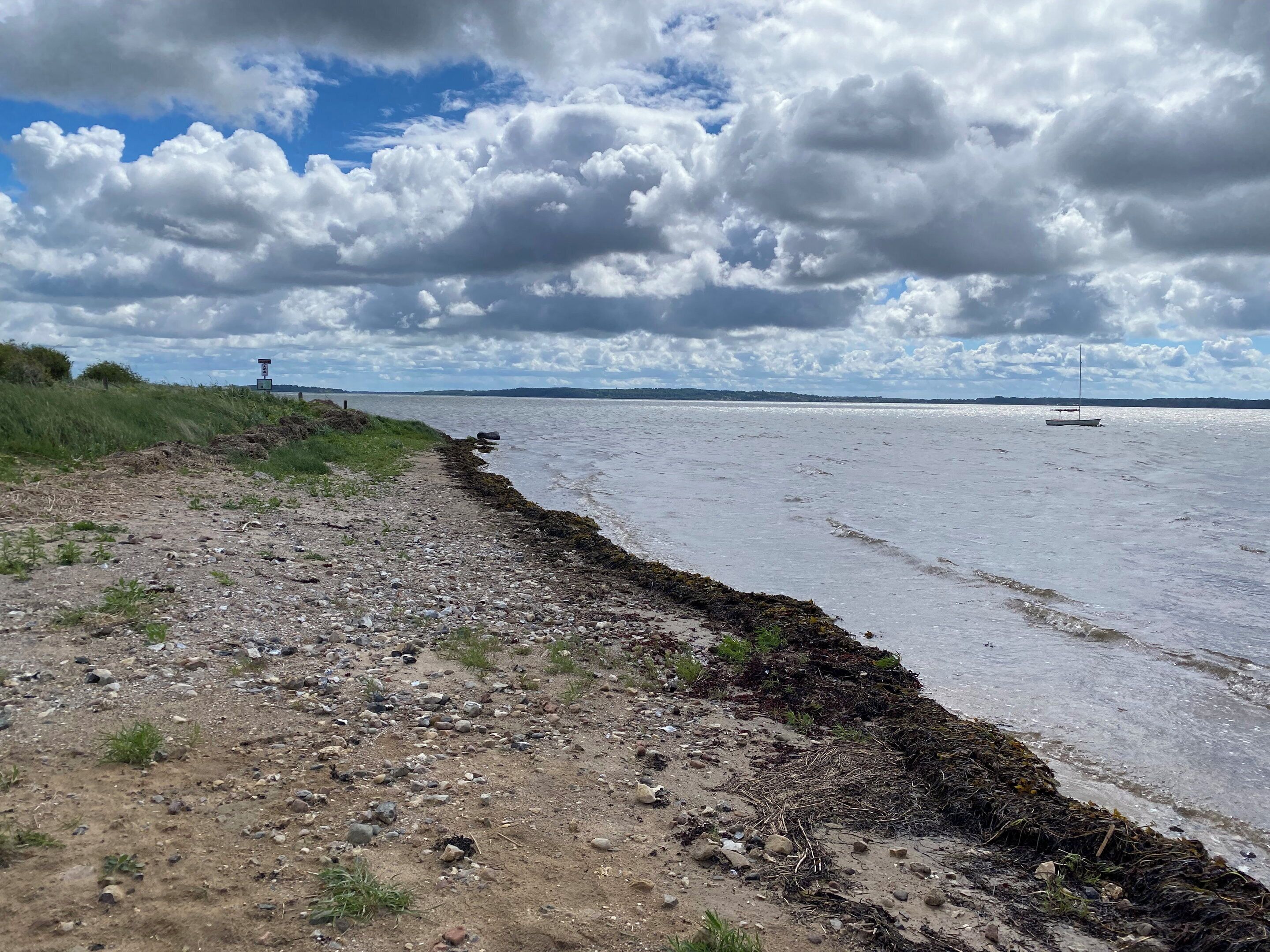 Un paysage côtier avec une rive rocheuse, un phare à l’horizon et un bateau sur l’eau.