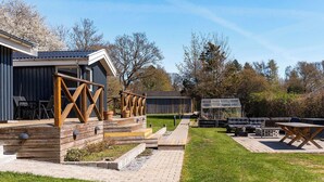 Ein moderner Außenbereich mit Holzdeck, Sitzgelegenheiten und einem Gewächshaus.