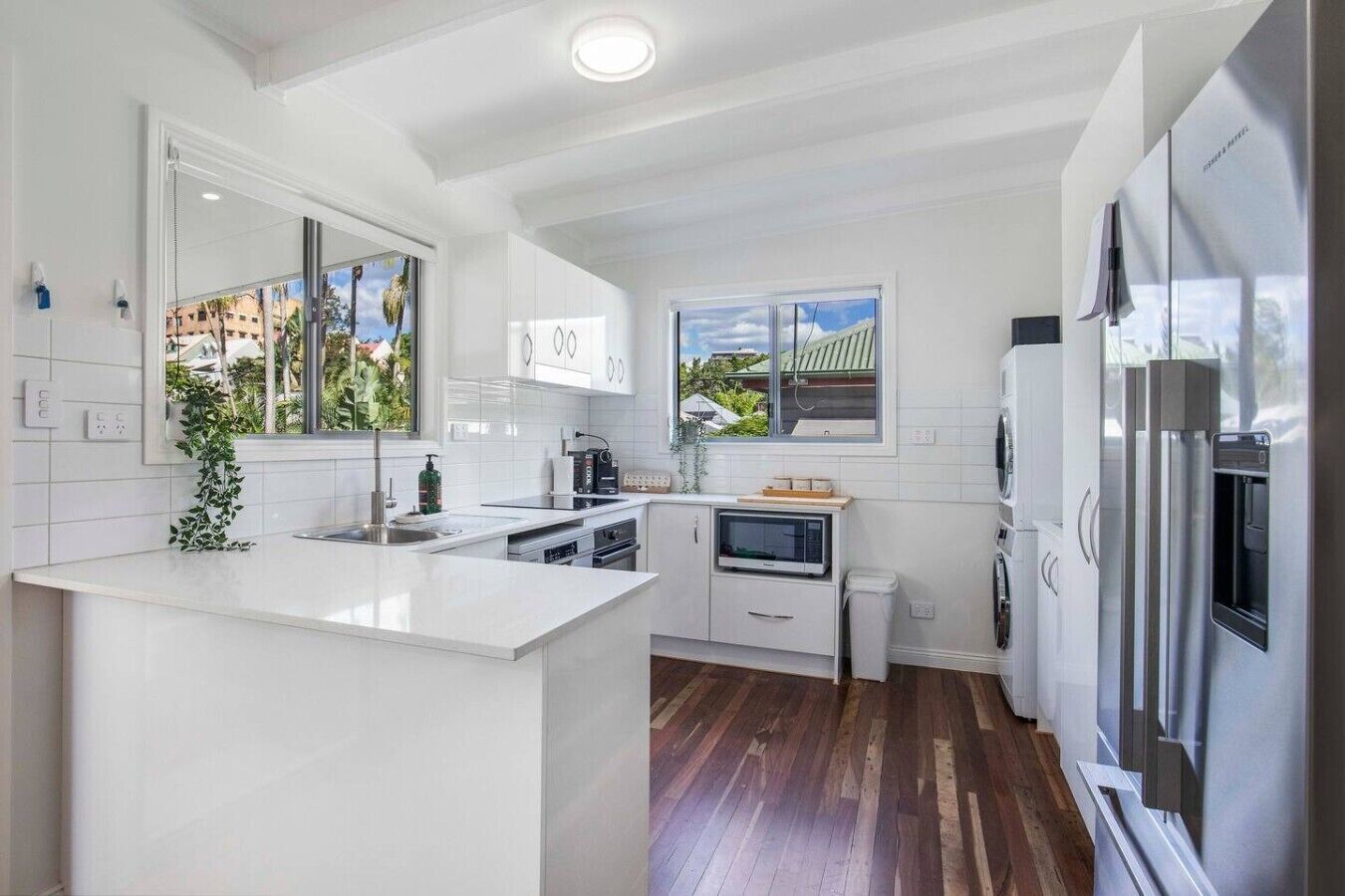 A modern kitchen with white cabinetry, a central island, stainless steel appliances, and a view of the neighborhood.
