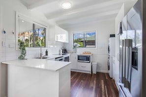 A modern kitchen with white cabinetry, a central island, stainless steel appliances, and a view of the neighborhood. - Central Retreat - 4Bed (Petrie Terrace)