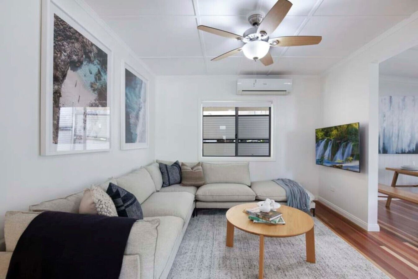 A living room with a sectional sofa, a round coffee table, a ceiling fan, and artwork on the walls.