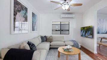 A living room with a sectional sofa, a round coffee table, a ceiling fan, and artwork on the walls.