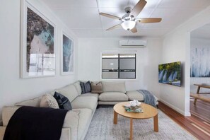 A living room with a sectional sofa, a round coffee table, a ceiling fan, and artwork on the walls. - Central Retreat - 4Bed (Petrie Terrace)