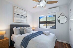 Un dormitorio con cama, ventilador de techo, ventana con vistas y espejo fijado a la pared.