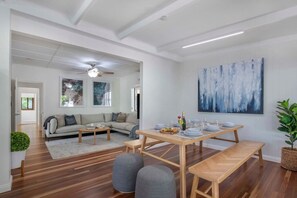 A modern living room with a sofa, a dining table set for four, and a large abstract painting on the wall. - Central Retreat - 4Bed (Petrie Terrace)