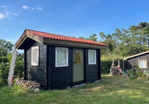 Une petite cabane en bois avec un toit rouge, deux fenêtres et une porte.