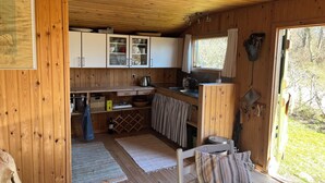 A wooden cabin interior with a kitchen area, including cabinets, a sink, and a window with curtains. - Beautifully situated classic wooden summercottage (Hadsund)