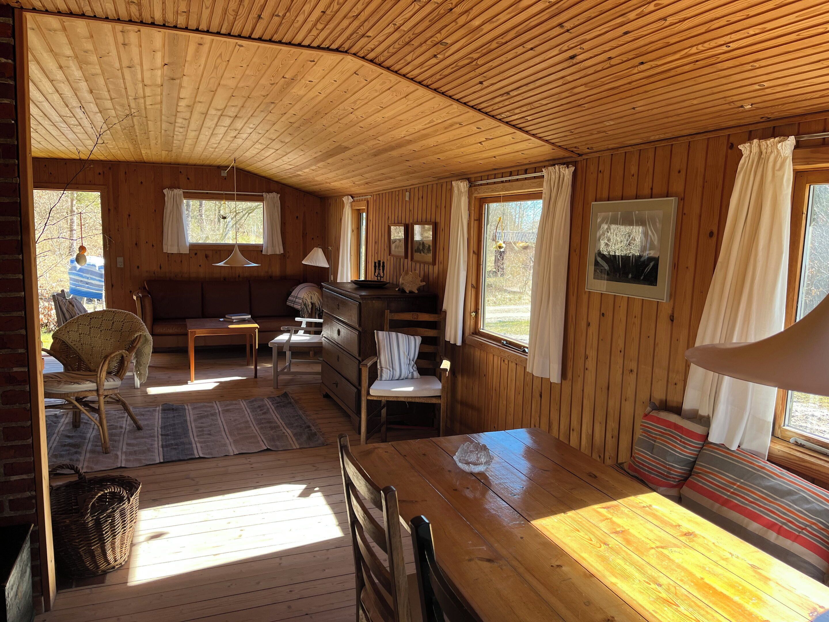 A wooden cabin interior with a dining table, chairs, a sofa, and a kitchen area.
