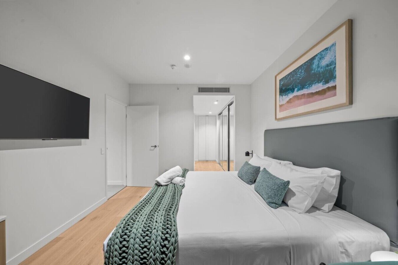 A modern bedroom with a large bed, a flat-screen TV, and a painting on the wall.