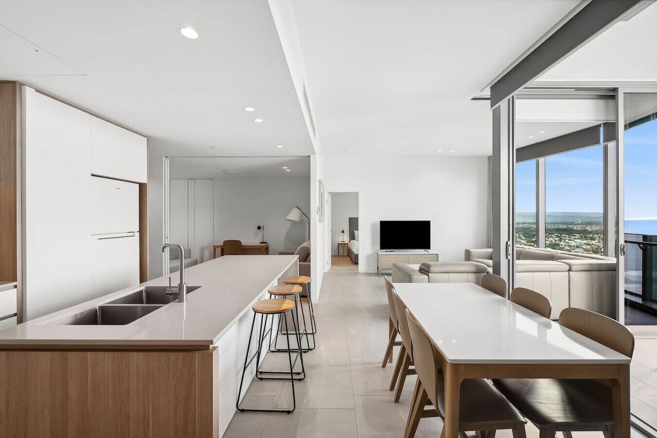 Uma cozinha moderna com ilha central, área de refeições com mesa e cadeiras grandes, e sala de estar com TV de tela plana e assentos.