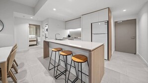 A modern kitchen with a central island, bar stools, a dining table, and a refrigerator.
