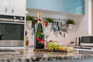 A bottle of G.H. Mumm champagne, a glass with a strawberry, grapes, and cheese on a wooden board in a modern kitchen. - 3BR Bulimba Family Retreat (Balmoral)