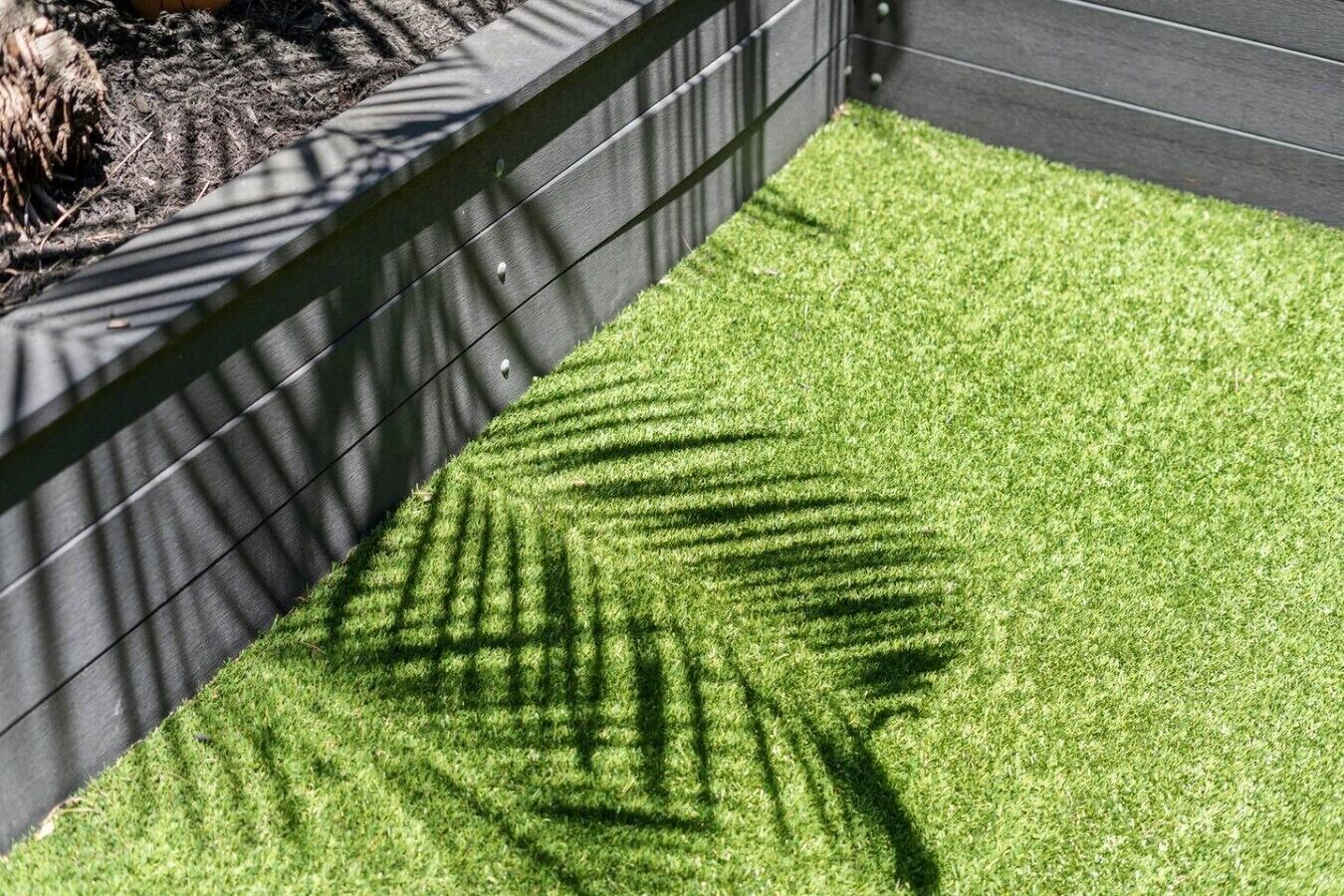A section of artificial grass with shadows cast by a structure, possibly a planter or planter box.