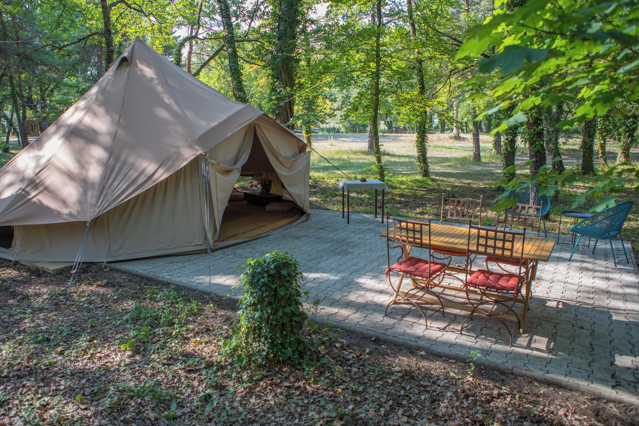 A tent set up in a forested area with a table and chairs nearby.