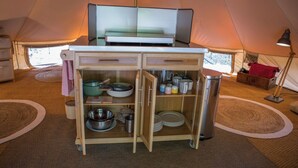 Een kleine keuken met een magnetron, fornuis en opbergkasten in een tent.