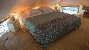 Een tent van binnen, met een bed, nachtkastje en een raam.