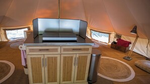 Een tent van binnen met een kitchenette, een afvalbak en een lamp.