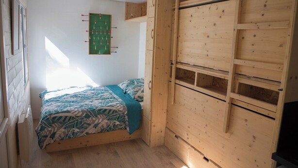 Ein Schlafzimmer mit einem Bett, einem Holzschrank und einem grünen Wandregal für ein Brettspiel.