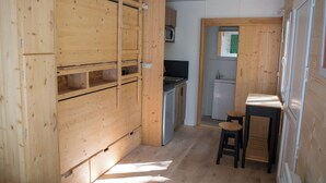 Eine kleine Küche mit Holzausstattung, einer Mikrowelle, einem Spülbecken und einem kleinen Hocker.