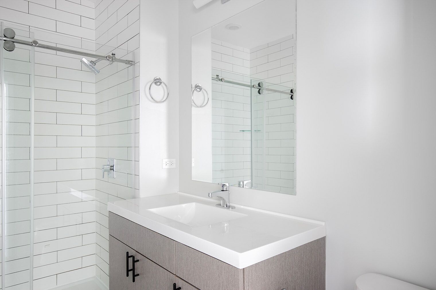 A modern bathroom with a white tiled shower, a double sink vanity, and a large mirror.