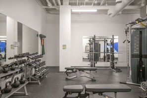 Een sportschool met gewichthefapparatuur, banken en een spiegelwand.