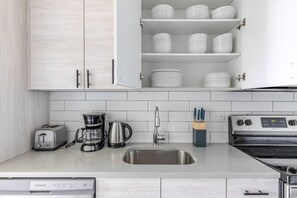 A kitchen with white cabinets, a stainless steel sink, a coffee maker, a toaster, and a stove. - Blueground | Edgewater, gym, nr Lake Michigan (Chicago)