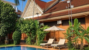 A traditional building with a tiled roof, a swimming pool, and lounge chairs. - ASANA (Siem Reap)