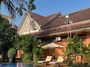 Un bâtiment traditionnel avec un toit en tuiles, une piscine et des chaises longues.
