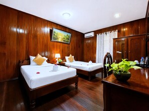 Une chambre d’hôtel avec deux lits en bois, un tableau au mur, un appareil de climatisation, un rideau et une table avec une plante.