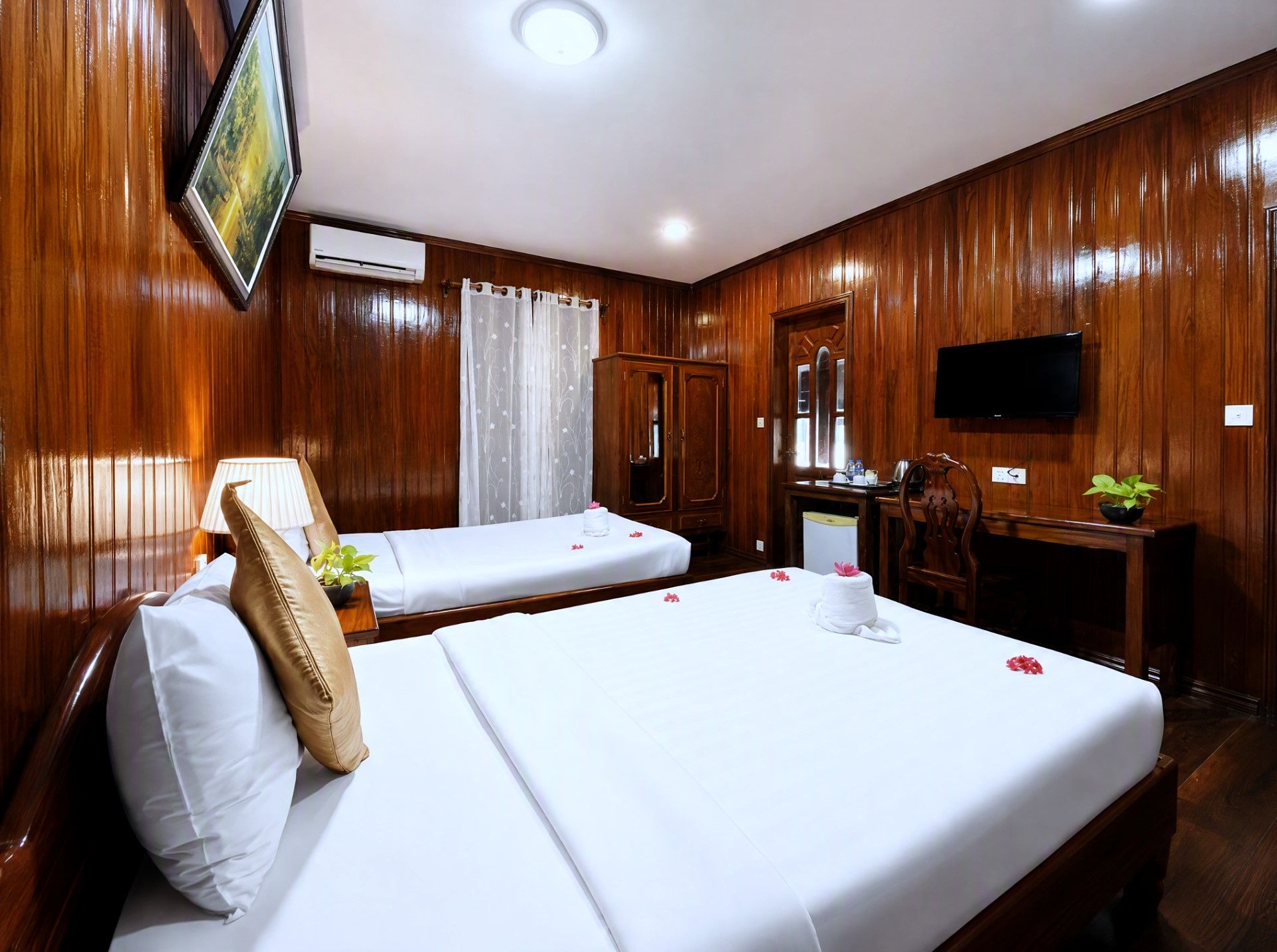 A hotel room with two beds, a desk, a television, and wooden paneling.