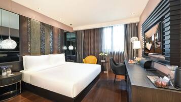 Quarto de hotel moderno com uma cama grande, uma escrivaninha com cadeira, televisão e um espelho amplo.