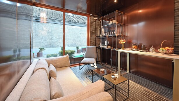 Een moderne woonkamer met een bank, een salontafel en een eethoek met een glazen vitrine en een keukenwerkblad.