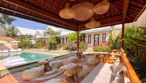 Un área junto a la piscina con una pérgola de madera, sillas de descanso y un letrero que dice 'Bacana'.