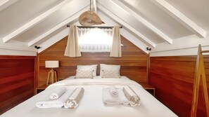 A hotel room with a wooden headboard, a bed with white linens, a standing lamp, and a ceiling fan.
