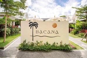 A sign with palm tree and sun icon, labeled 'BACANA' in a resort setting.