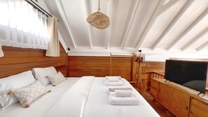 Une chambre à coucher avec une tête de lit en bois, un grand lit avec du linge de lit blanc, un luminaire suspendu, une commode en bois et un téléviseur.