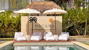 A pool area with a sign reading "BACANA" and several white cushions.
