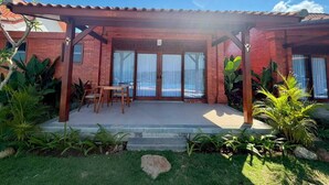 Une terrasse couverte avec un bâtiment en briques, une piscine et des plantes tropicales.
