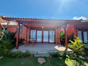 Un patio techado con un edificio de ladrillo, una piscina y plantas tropicales.