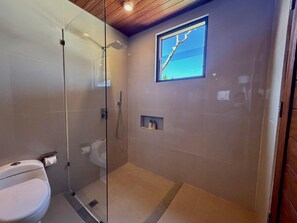 Un baño moderno con cabina de ducha de vidrio, inodoro y un pequeño estante con artículos de aseo.