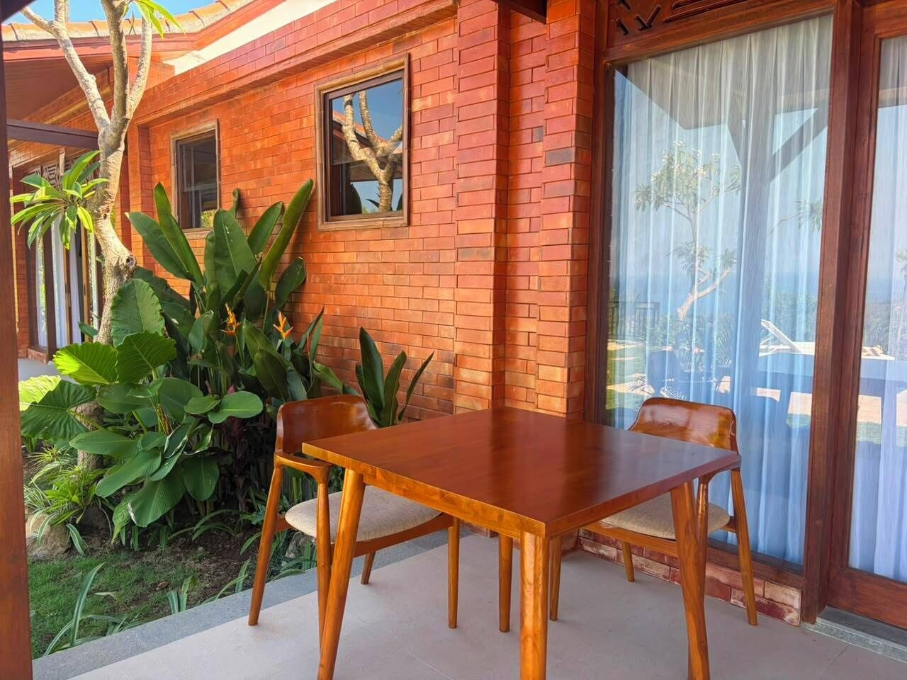 A patio with a wooden table and chairs, surrounded by plants and a brick wall.