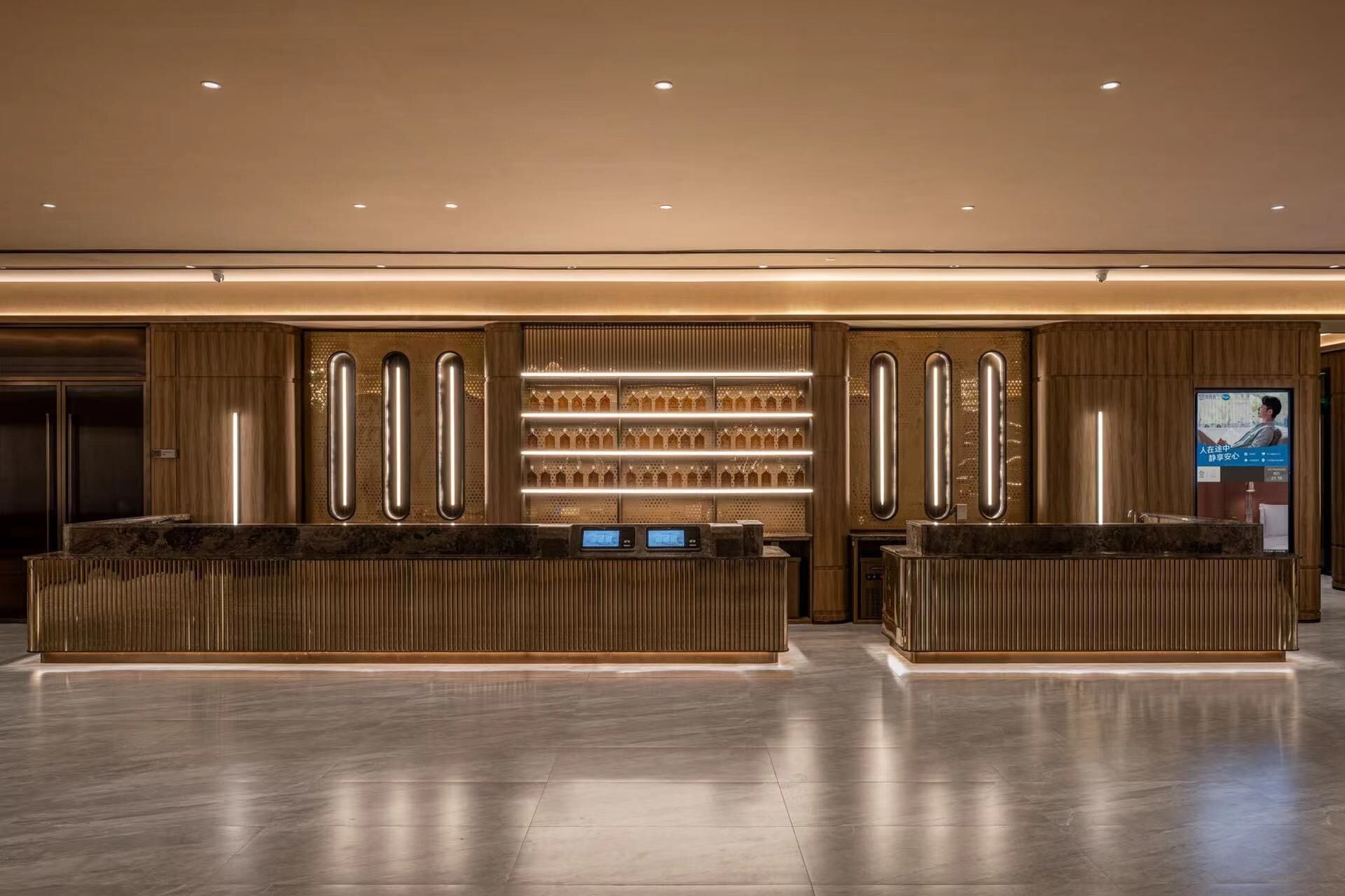 Un área de recepción moderna con un mostrador central, una pantalla digital y una estantería con vasos.